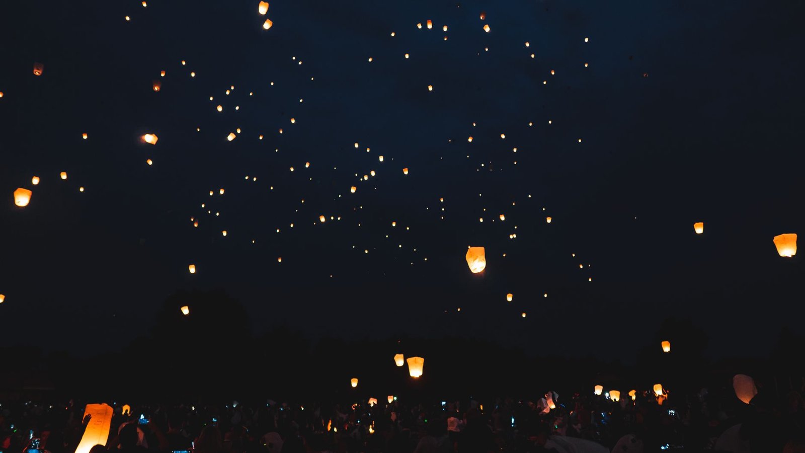 Numerous floating lanterns light up the night sky during a cultural festival, creating a serene and ethereal atmosphere