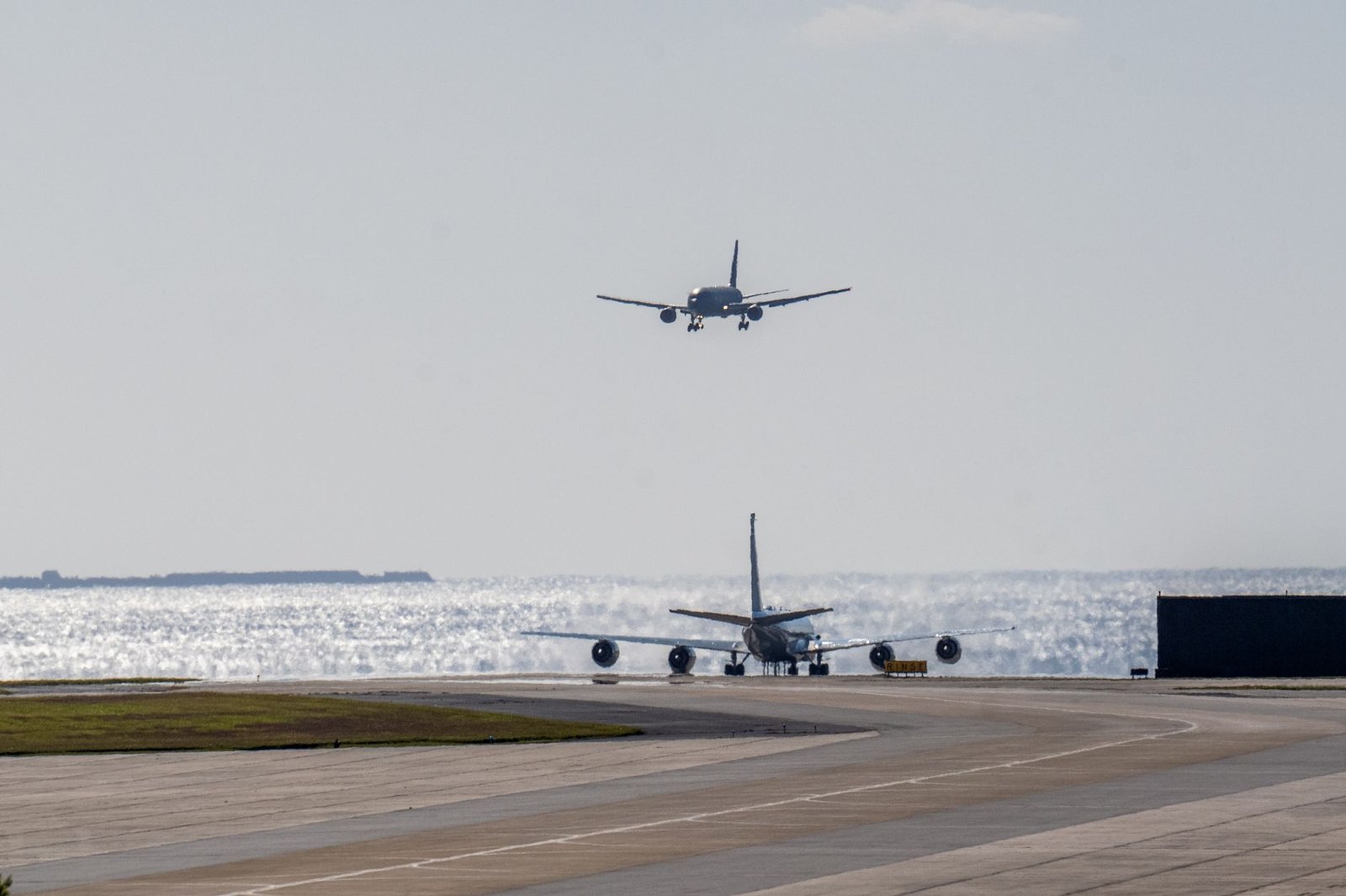 Two airplanes on a sunny runway by the sea, one landing and the other on ground