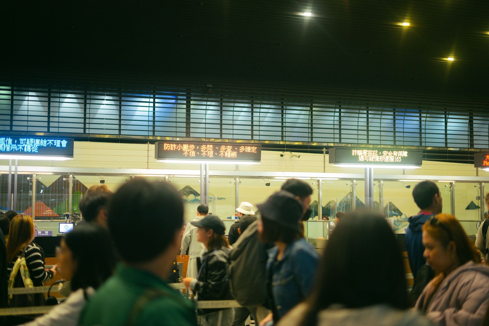 Crowded airport check-in area with people queueing and visible flight information signs
