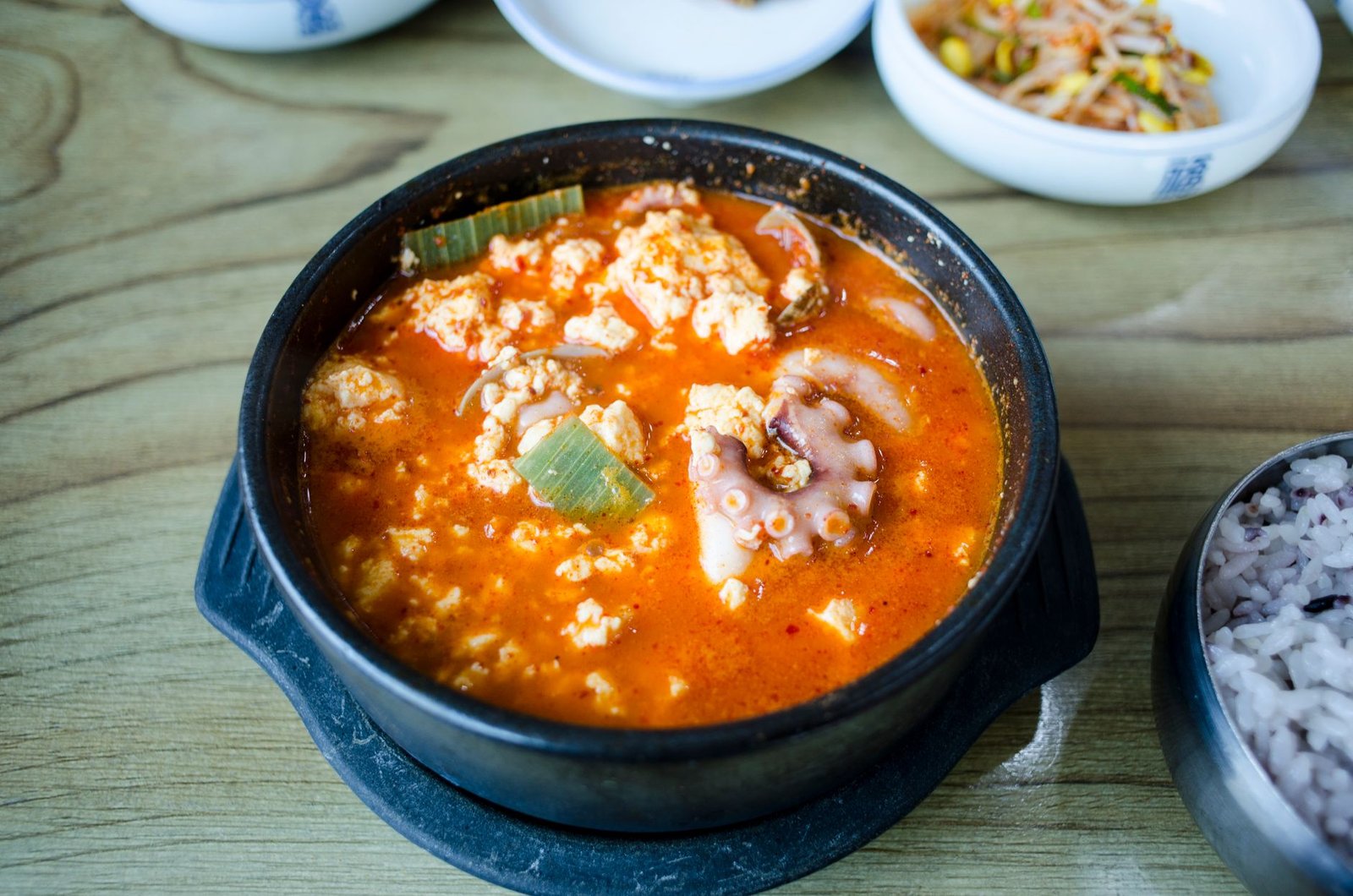 A delicious spicy Korean tofu soup served hot in a black stone bowl with side dishes