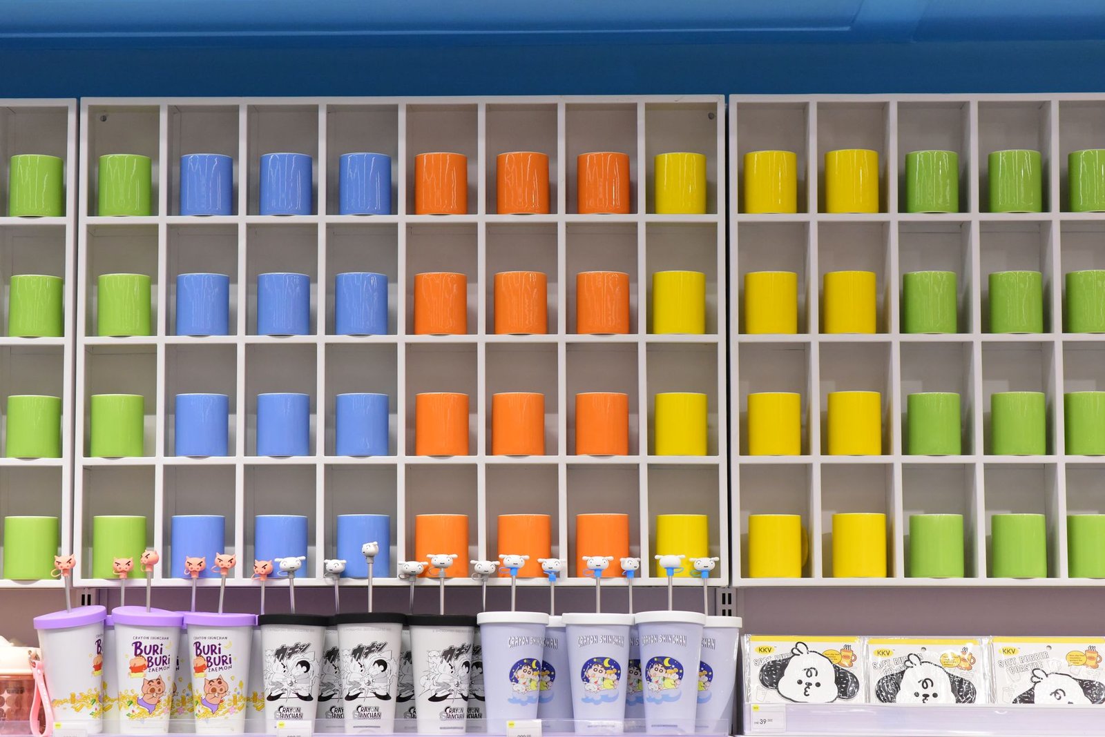 Vibrant shelf of colorful cups in a retail store, organized by color and showcasing a playful design