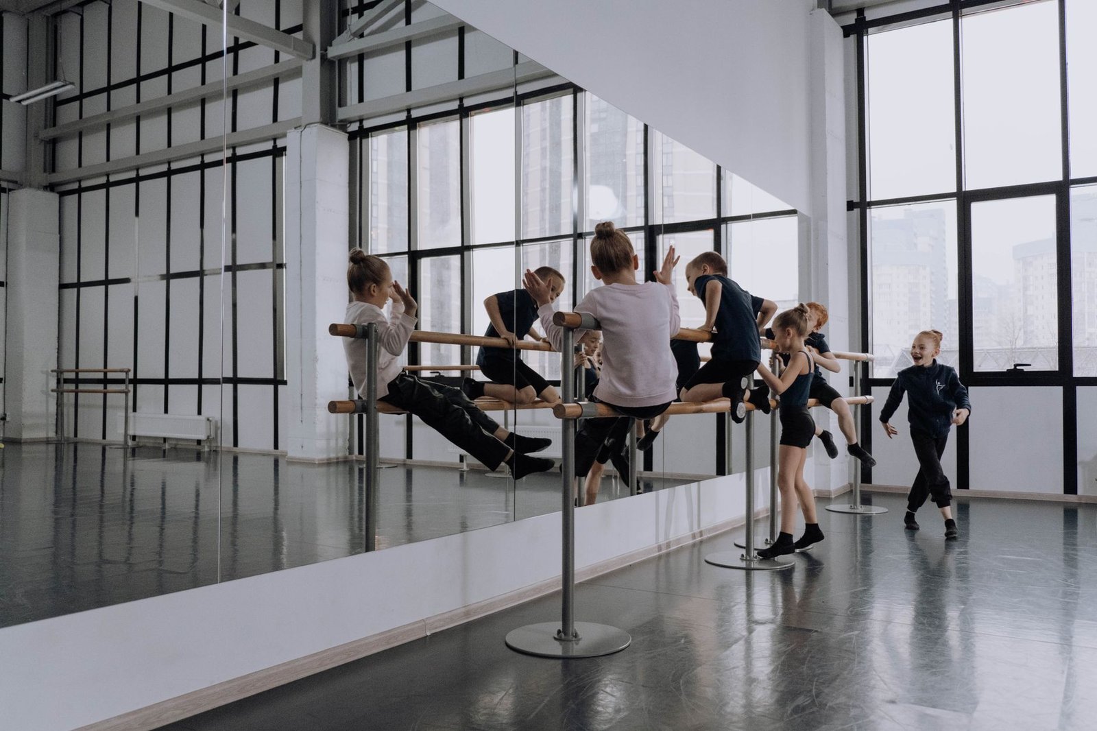 Kids engaging in ballet practice in a modern dance studio with large mirrors and natural light
