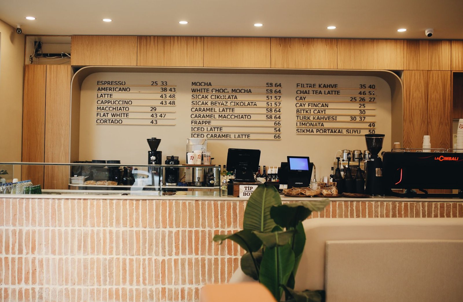 Warm café interior featuring a detailed coffee menu and counter setup with plants