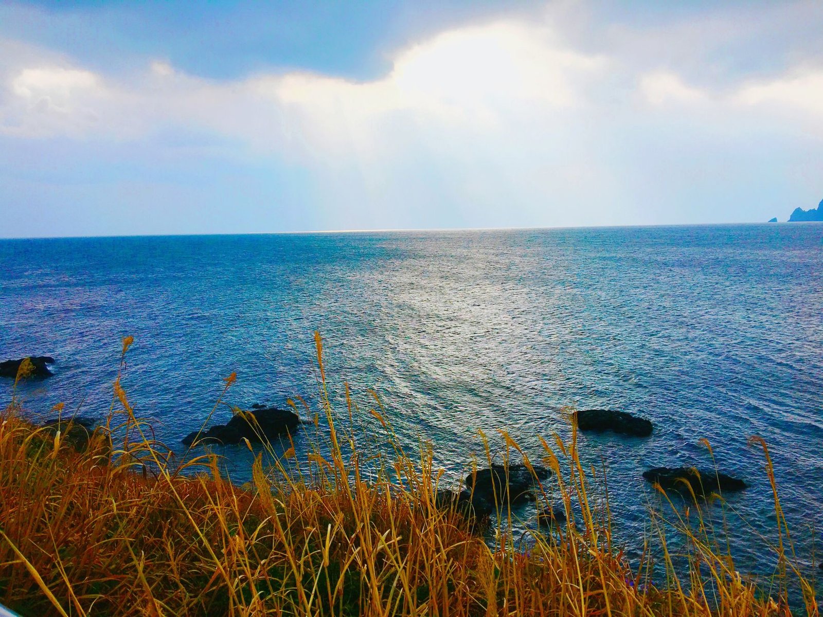 Serene ocean view from Jeju Island, South Korea, with sun rays breaking through clouds